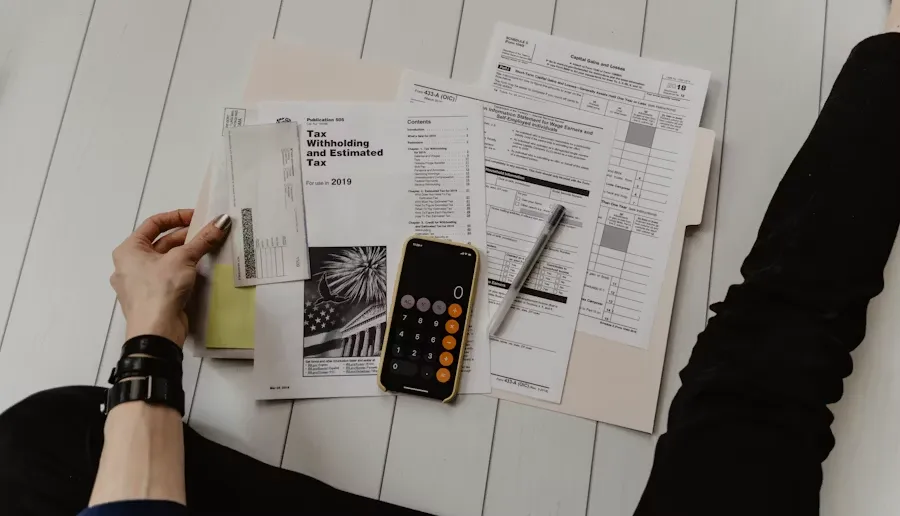 Overhead view of a person organizing tax documents with a smartphone, calculator app, and a pen on a white desk.